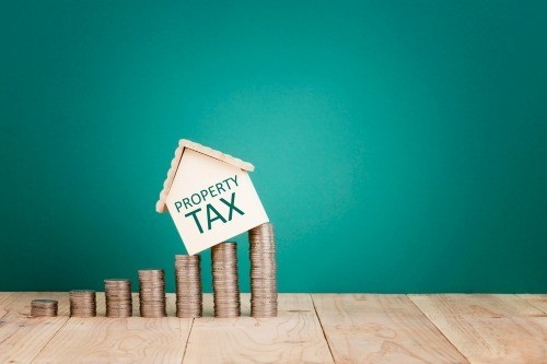 Rising property tax depicted by a small wooden house stacked on coins shaped like a rising bar chart