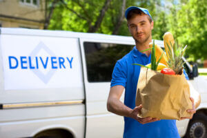 Man holding a bag of groceries in front of a delivery van